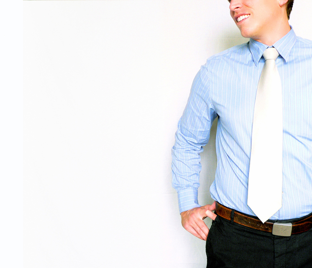 Muž v modrej košeli s kravatou stojí vedľa bielej steny